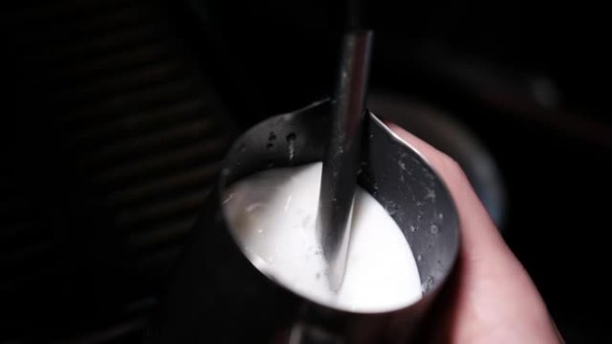 为卡布奇诺或拿铁制备牛奶泡沫，加热和搅打的过程。咖啡师在水罐里蒸牛奶。慢动作