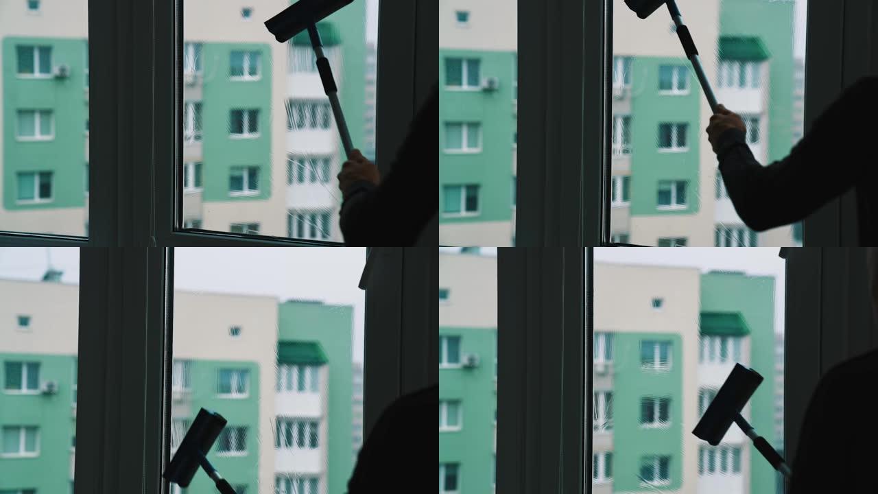 在城市的家里洗窗户的过程。一名男子用刷子和特殊液体清洁玻璃窗的轮廓，放在高高的建筑背景上。