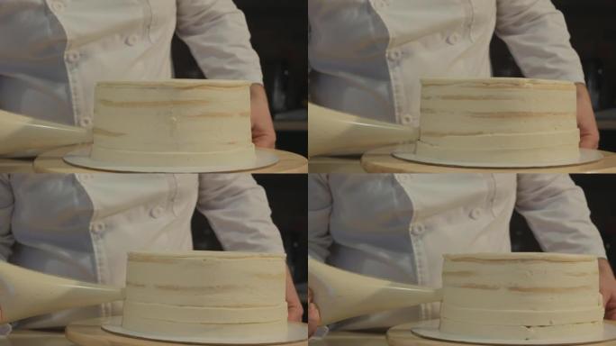男人糕点厨师穿着白色衣服创造了蛋糕的形状。他将奶油从冷却器中压到蛋糕坯的侧面。甜点