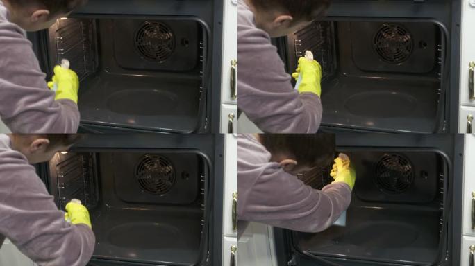 妇女在厨房做饭后戴着橡胶手套清洁烤箱，用烤箱清洁剂喷洒并用布擦拭。