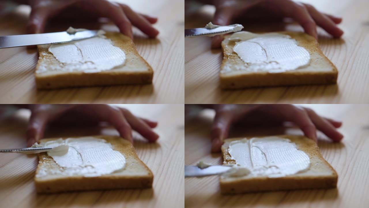 涂抹黄油三明治。女性双手用涂抹奶油黄油慢动作制作烤面包三明治。烤面包和在桌子上涂抹黄油。