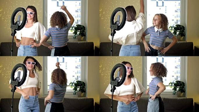 开朗的年轻女子和她十几岁的女儿积极跳舞，情绪激动，在镜头前玩得开心，在家中用三脚架上的手机拍摄视频，