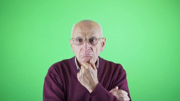 忧郁的退休人员戴着眼镜，用手在绿色背景上握着下巴
