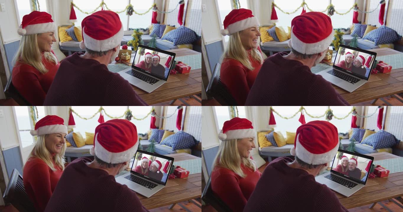 带着圣诞老人帽子微笑的高加索夫妇使用笔记本电脑进行圣诞视频通话屏幕上的夫妇