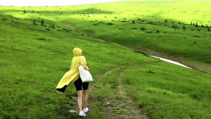 穿着鲜黄色外套的女徒步旅行者在乡村山区旅行。绿浪山