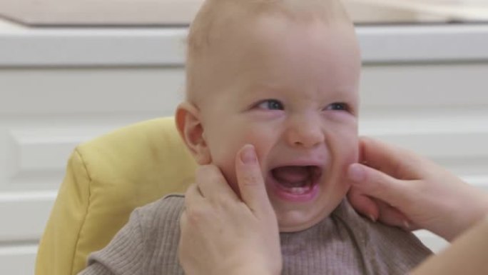 快乐的妈妈带着微笑的宝宝在家，慈爱的妈妈挤压宝宝的脸颊，8个月大的高加索孩子的脸特写。