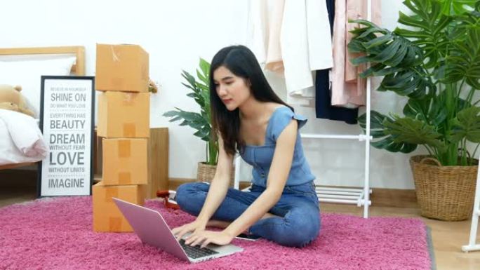 4K。亚洲妇女在带包装箱的卧室地板上的计算机笔记本上打字键盘。电子商务，网上购物，网上零售时装店，小