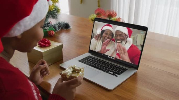 戴着圣诞老人帽子的非洲裔美国妇女使用笔记本电脑进行圣诞节视频通话，屏幕上有情侣