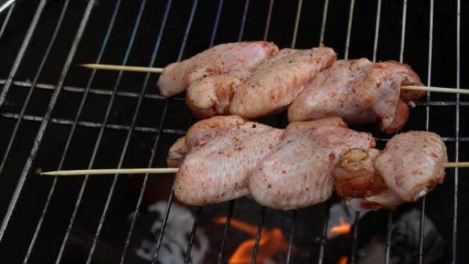 木串上的生鸡翅放在烤架上的明火上方