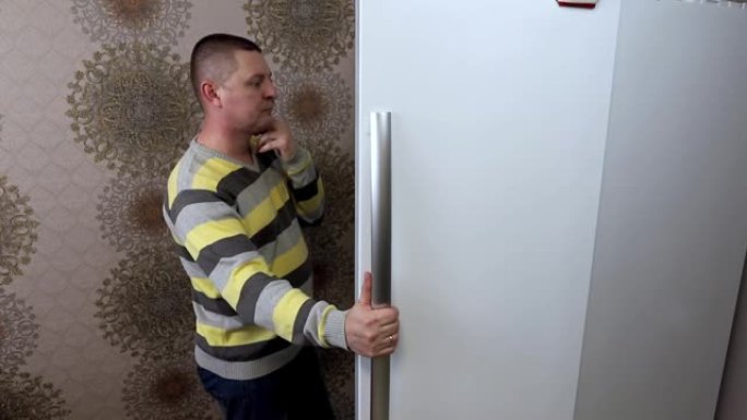 一个男人打开厨房的冰箱，长时间选择吃什么食物