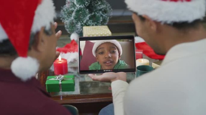 带有圣诞老人帽子的混血儿父子使用平板电脑进行圣诞节视频通话，屏幕上有男孩