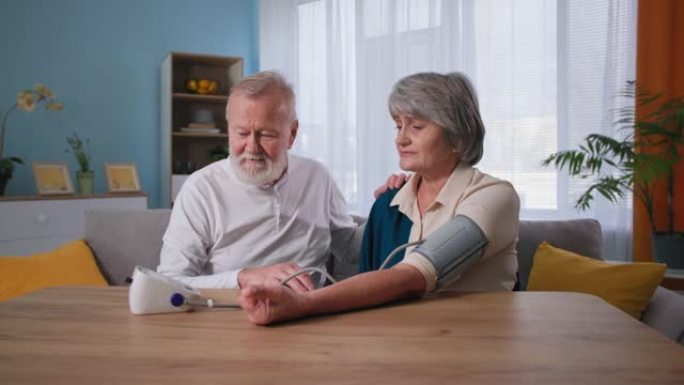快乐的养老金领取者照顾自己的健康，有爱心的丈夫用眼压计在家中给老妻子测量血压