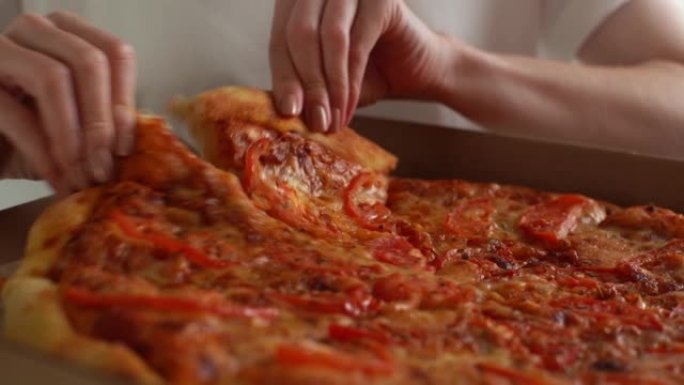 无法辨认的年轻成年妇女的特写手从纸板打开盒中取出一块热美味的意大利披萨，送餐服务。