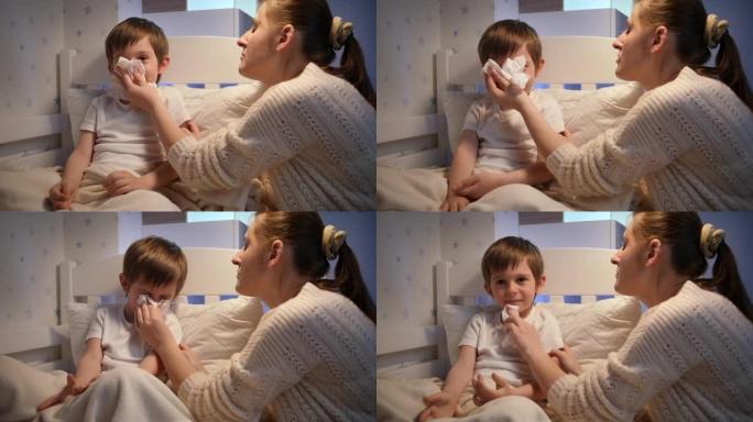 有爱心的母亲在床上吹着生病的小儿子流鼻涕。儿童疾病、疾病和父母护理的概念