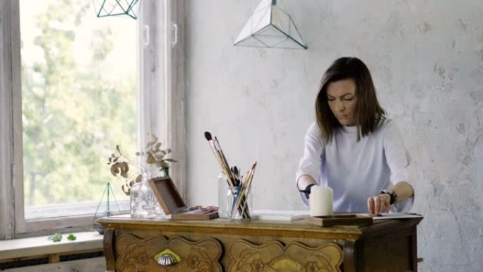 一位漂亮的黑暗女性艺术家在她的木桌上用铅笔在纸上画画。4K