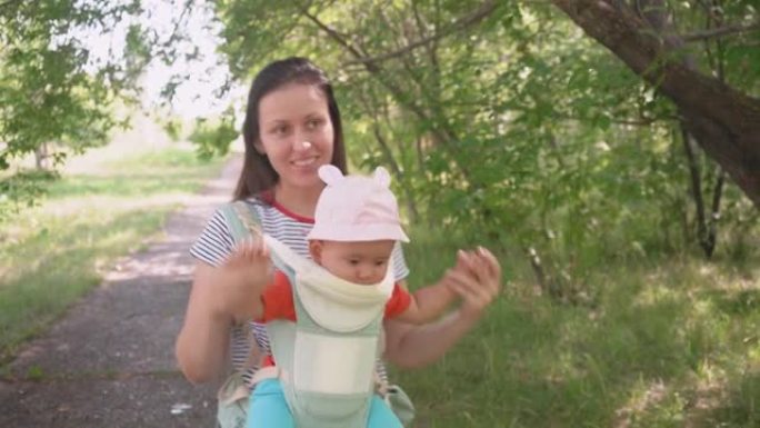 一位母亲带着刚出生的婴儿在吊带上散步穿过夏季公园，探索他们周围的世界。