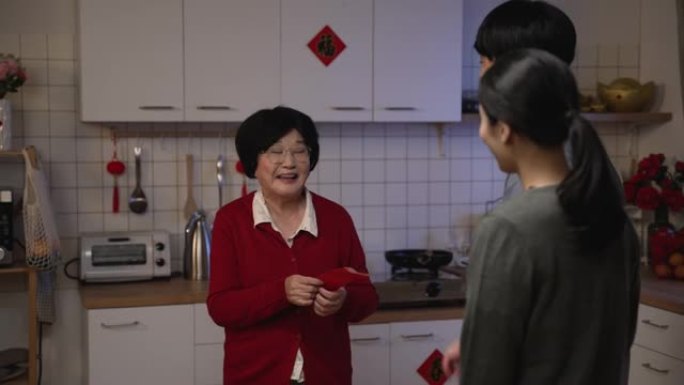 快乐的亚洲老母亲，红着脸，尴尬地笑着，接受成年儿媳在厨房里吃完晚饭后的压岁钱