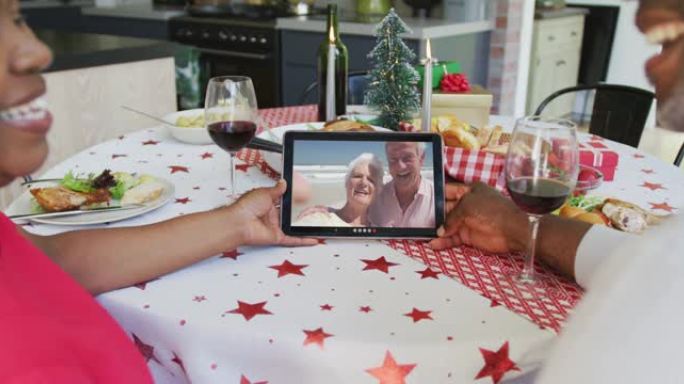 微笑的非洲裔美国夫妇使用平板电脑与屏幕上的幸福夫妇进行圣诞节视频通话