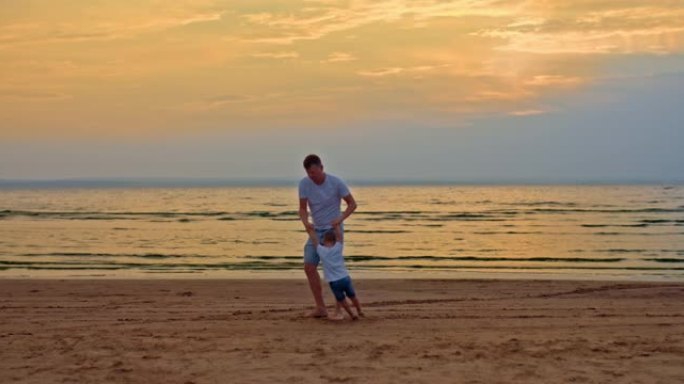 慈爱的父亲双手盘旋着儿子，在海边散步。爸爸和他的小儿子在沙滩上玩耍，他们玩得很开心。快乐的父亲和童年
