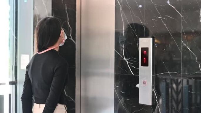 戴口罩和按下电梯按钮的聪明亚洲女商人