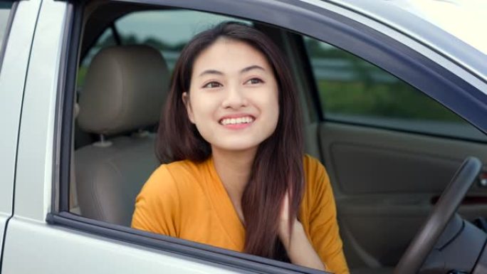 年轻漂亮的亚洲女性得到新车。她看着窗外非常高兴和兴奋。灿烂的日子里，微笑的女性驾驶车辆在路上