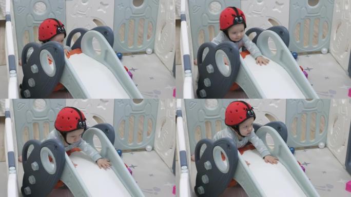 戴着婴儿安全帽的可爱蹒跚学步享受婴儿滑梯游戏围栏的游戏时间，8个月大的男婴在安全活动中心玩耍。