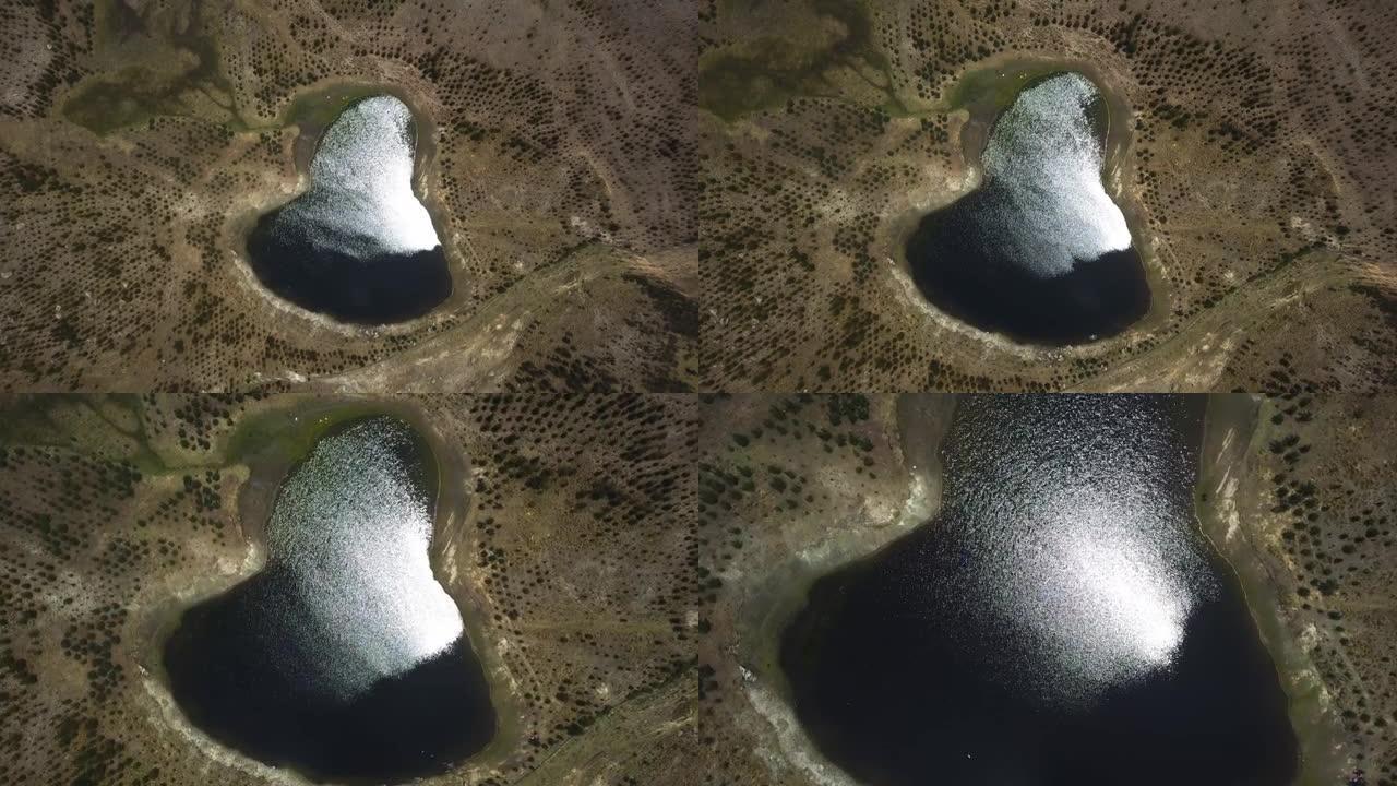 从梨形弧度泻湖上方的空中无人机视图，太阳对水的反射接近并从秘鲁瓦拉斯高地的内部溅水
