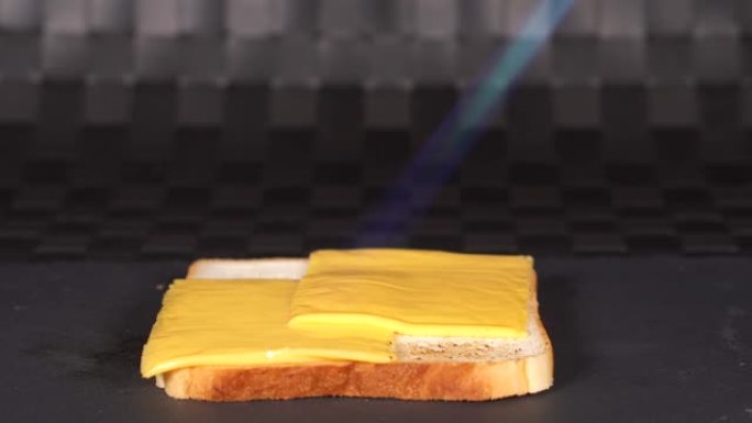 用燃烧器在方形吐司上融化的奶酪。火使白面包三明治上的奶酪变暖。烹饪过程的特写。