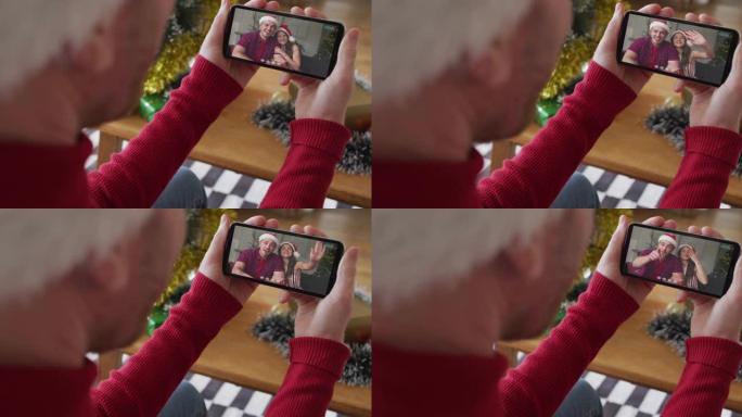 戴着圣诞老人帽子的白人男子使用智能手机进行圣诞节视频通话，屏幕上有微笑的情侣