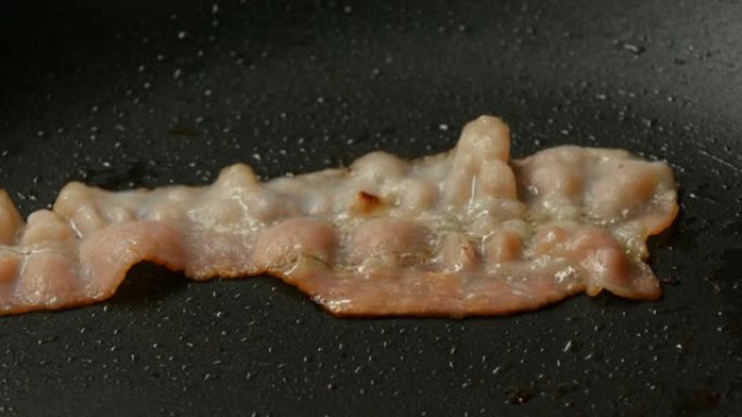 在热锅中用葵花籽油油炸一片培根，并带有不粘涂层特写视图