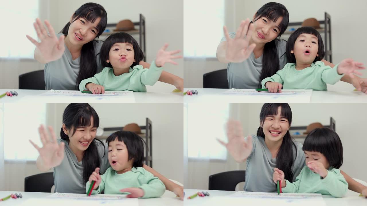 快乐时刻亚洲母亲和小男孩在家里用蜡笔画画时对相机打招呼或再见。家人在房子里玩得开心。妈妈教儿子作业。