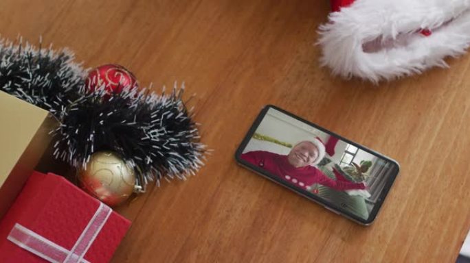 微笑的白化非洲裔美国男子戴着圣诞老人的帽子，在智能手机上播放圣诞节视频通话
