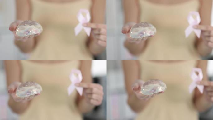 女病人手持硅胶乳房植入物和粉红色丝带特写4k电影慢镜头