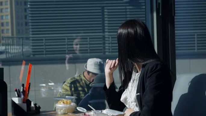 女商人在工作场所吃饭，在全景窗户附近的现代漂亮办公室里，与窗户里的工人，建筑商调情