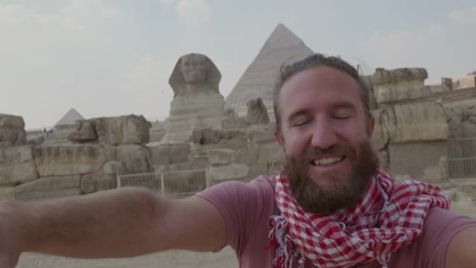 慢动作: 年轻人旅行在吉萨大金字塔前自拍。男性在埃及开罗与金字塔和狮身人面像一起自拍