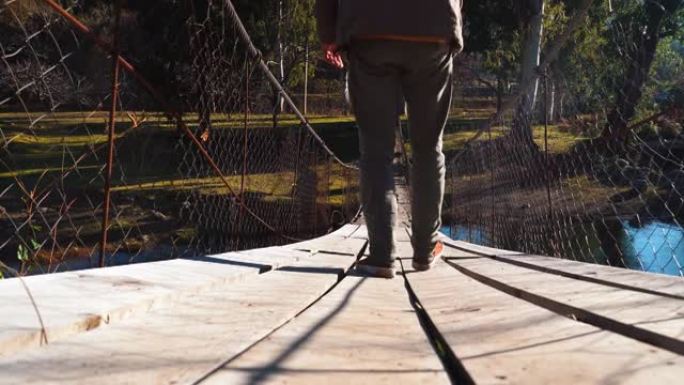 一个年轻的男性游客走在一座悬挂的木桥上，
