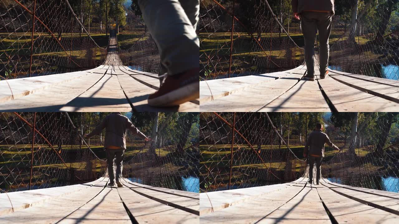 一个年轻的男性游客走在一座悬挂的木桥上，