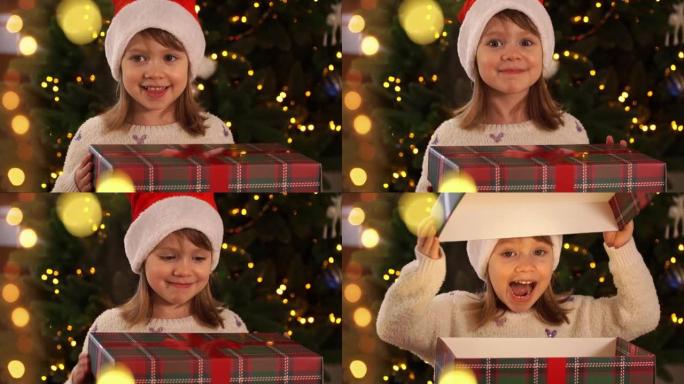 穿着红色圣诞老人帽子的快乐小女孩打开礼品盒，魔灯在圣诞树的背景上惊讶和大笑。新年