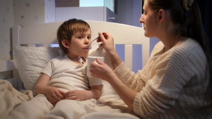 生病的小男孩感到不适躺在床上，喝着勺子里的药和糖浆。儿童疾病、疾病和父母护理的概念
