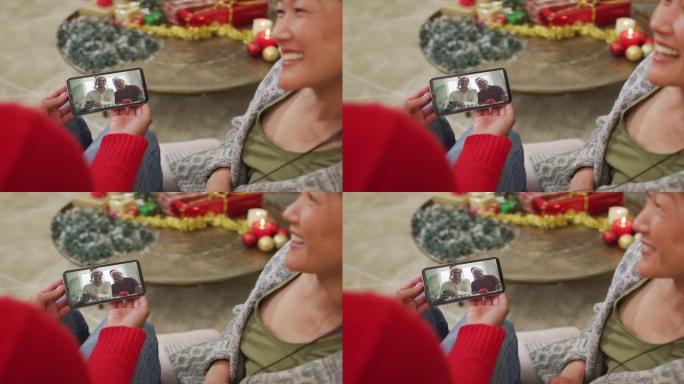 微笑的亚洲夫妇使用智能手机与屏幕上的幸福家庭进行圣诞节视频通话