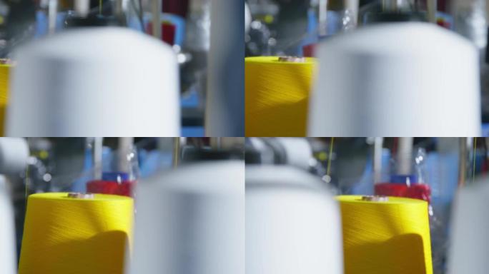 带有彩色螺纹的大型线轴安装在生产工厂的机器人机器上，靠近，模糊的前景。缝纫过程中黄线被解开