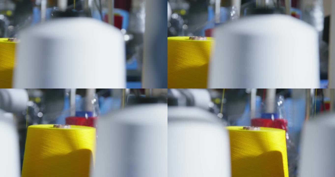 带有彩色螺纹的大型线轴安装在生产工厂的机器人机器上，靠近，模糊的前景。缝纫过程中黄线被解开