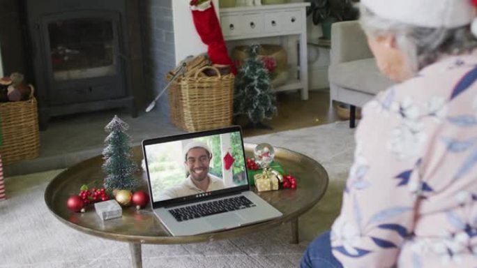 戴着圣诞老人帽子的高加索高级女性使用笔记本电脑进行圣诞视频通话，屏幕上有男人