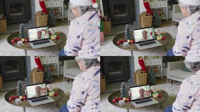 戴着圣诞老人帽子的高加索高级女性使用笔记本电脑进行圣诞视频通话，屏幕上有男人