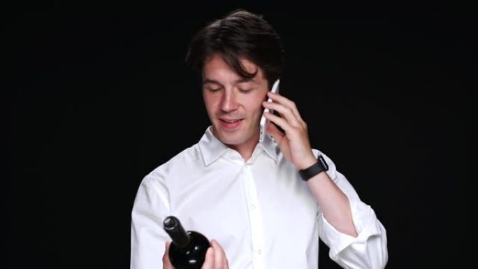 英俊的黑发男人拿着一瓶葡萄酒和电话交谈
