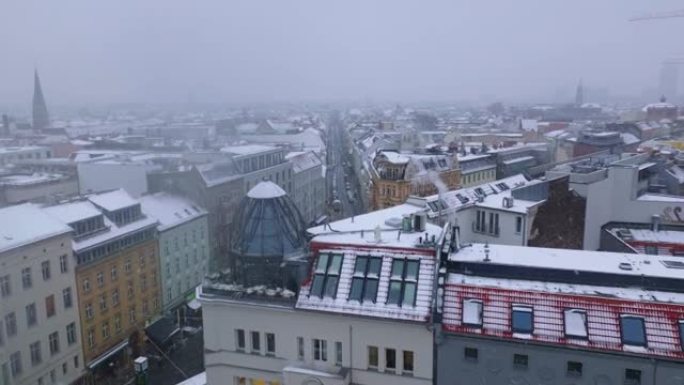 在镇上角落的房子里滑动和平移屋顶玻璃冲天炉的镜头。城市社区下雪。背景中的建筑起重机。德国柏林