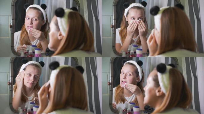 年轻女子在浴室镜子里看着自己，用海绵用乳液擦拭脸上的红肿。脸上有红肿和丘疹。健康、美容、皮肤治疗
