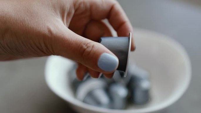 人从厨房的白色盘子里拿出一个小的银色胶囊，用于自动咖啡机。早上早餐