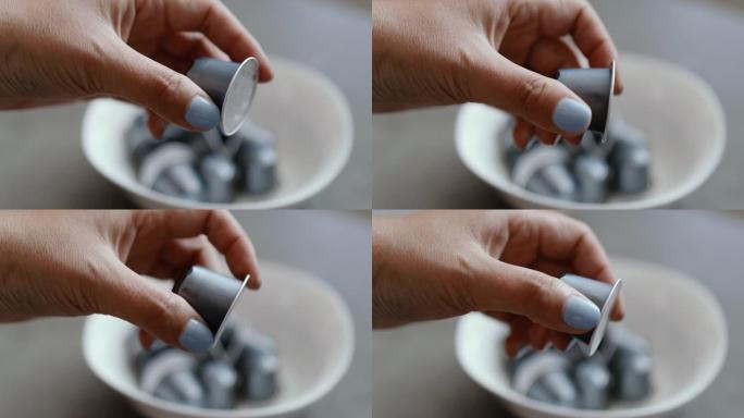 人从厨房的白色盘子里拿出一个小的银色胶囊，用于自动咖啡机。早上早餐