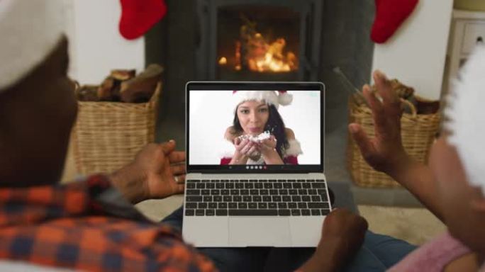 非裔美国人夫妇戴着圣诞老人帽子，使用笔记本电脑与屏幕上的女人进行圣诞节视频通话